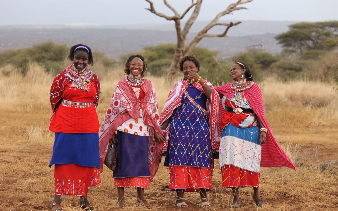 A group of Maasai women smile and pose for a photo wearing traditional attires.