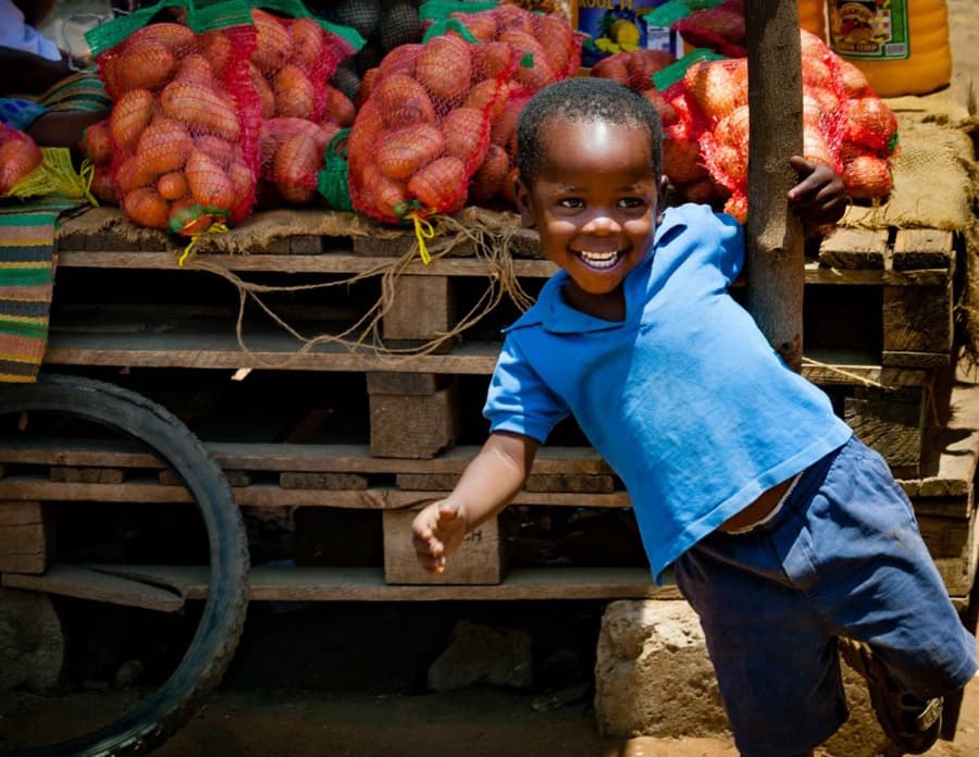 Image of a boy smiling outside in front of a vegetable cart